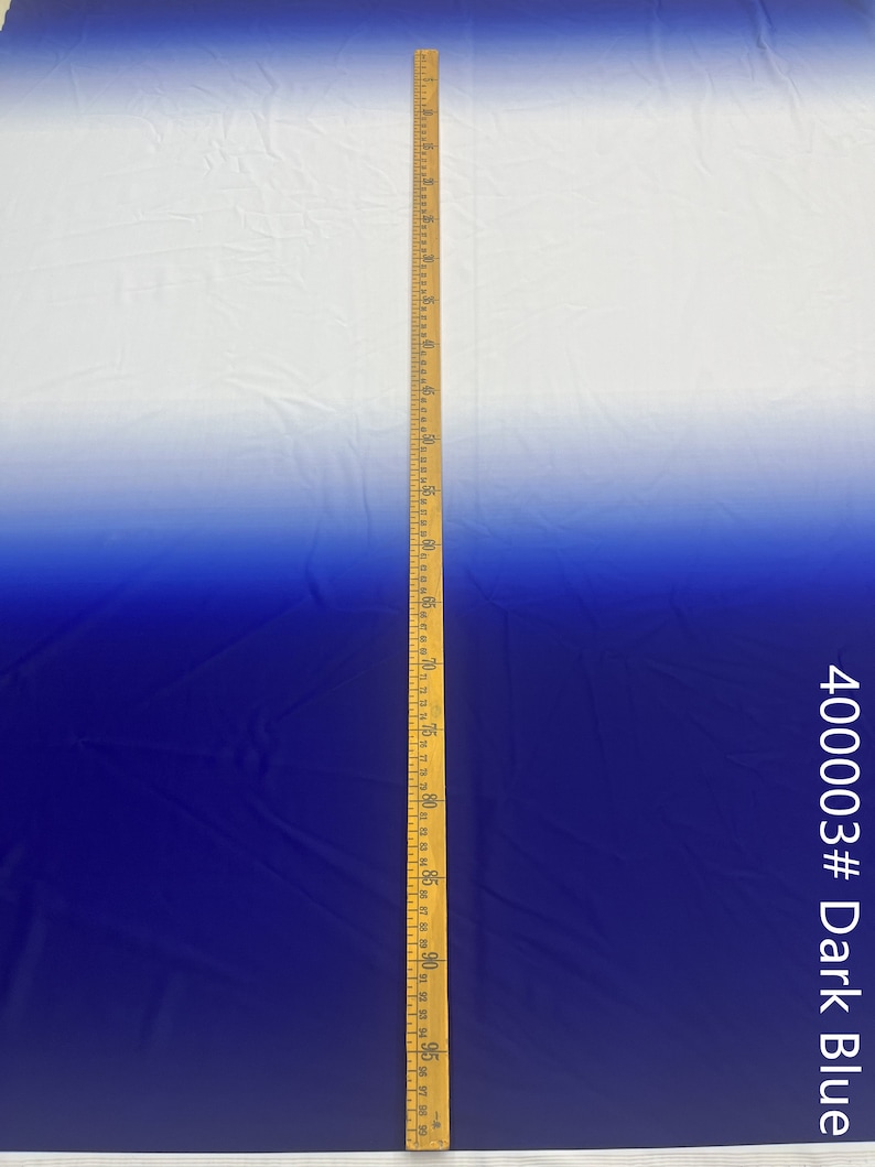 May include: A white to dark blue ombre fabric with a wooden ruler measuring 96 inches. The fabric is smooth and has a slight sheen. The fabric is labeled "400003# Dark Blue".