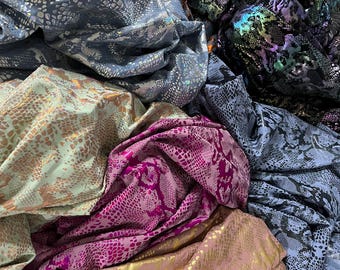 May include: A collection of fabric swatches in various snake skin patterns. The swatches are in shades of blue, green, pink, gold, and brown.