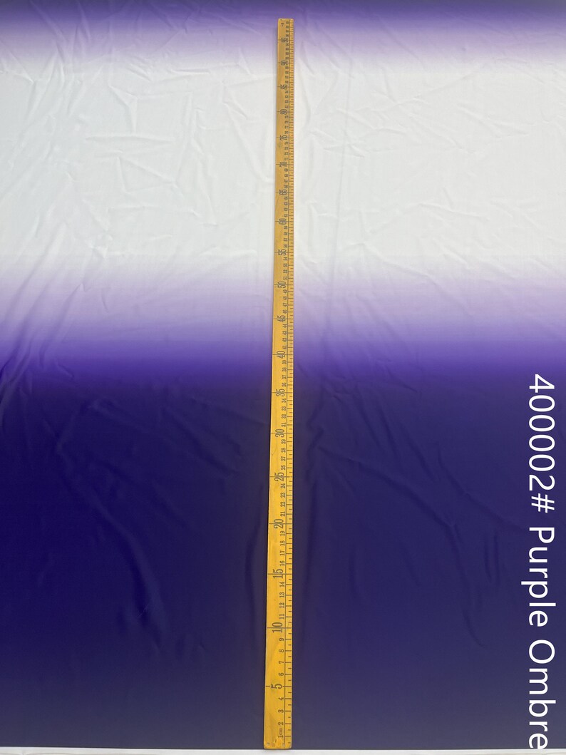 May include: A white to purple ombre fabric with a ruler measuring 60 inches. The fabric is smooth and has a slight sheen. The fabric is labeled 400002# Purple Ombre.