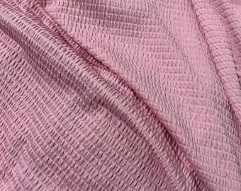 May include: Pink textured fabric with a waffle-like pattern. The fabric is soft and has a subtle sheen.