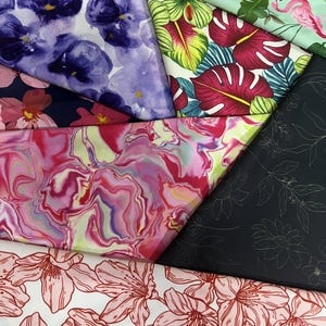 May include: A collection of double side brushed polyester spandex fabric swatches featuring various prints including purple pansies, pink flamingos with tropical leaves, a pink and purple marble pattern, black with white line art flowers, and white with red floral outlines.