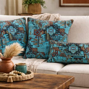 Peut inclure: Ensemble de trois coussins décoratifs avec un motif géométrique turquoise et marron. Les coussins sont sur un canapé beige. Un plateau décoratif avec un vase et d'autres éléments de décoration est posé sur une table basse en bois.