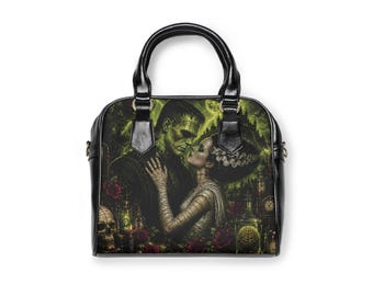 May include: A black handbag featuring a graphic print of Frankenstein's monster and his bride in a green-toned, atmospheric setting. The design includes a skull, red roses, and a castle silhouette, with black handles and gold-toned hardware accents.