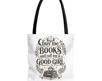 May include: A white tote bag with black handles featuring a black ink illustration of a stack of books, a steaming cup, and the text 'buy me BOOKS and call me a GOOD GIRL' surrounded by floral vines, stars, and a crescent moon design.