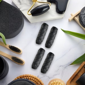 May include: Six black charcoal floss picks on a white marble surface. The floss picks are individually wrapped and have a woven texture.