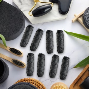May include: Ten black charcoal floss picks arranged in two rows on a white marble surface. The floss picks are made of woven charcoal fibers and are designed for cleaning between teeth.
