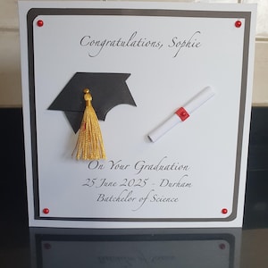 May include: A graduation card featuring a black mortarboard with a gold tassel and a rolled diploma. The card is inscribed with "Congratulations, Sophie" and "On Your Graduation 25 June 2025 - Durham Bachelor of Science". Red dots adorn the corners.