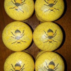 May include: Six yellow wooden knobs with a distressed finish. Each knob features a black and yellow bee with wings.