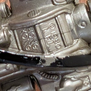 Peut inclure: Gros plan sur un robot jouet argent&eacute; avec des d&eacute;tails noirs. Le robot a une surface textur&eacute;e et les mots "L.L.B.O.  KING" sont visibles sur la poitrine.