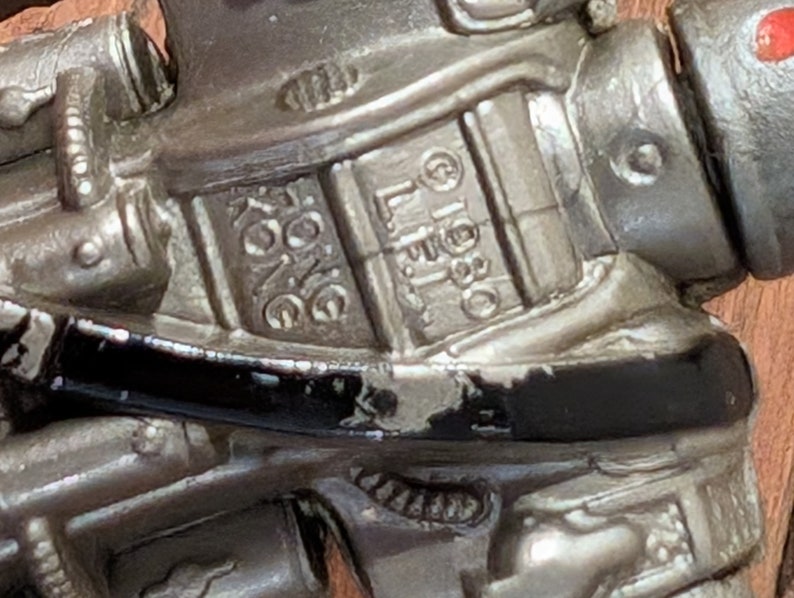 Peut inclure: Gros plan sur un robot jouet argent&eacute; avec des d&eacute;tails noirs. Le robot a une surface textur&eacute;e et les mots "L.L.B.O.  KING" sont visibles sur la poitrine.
