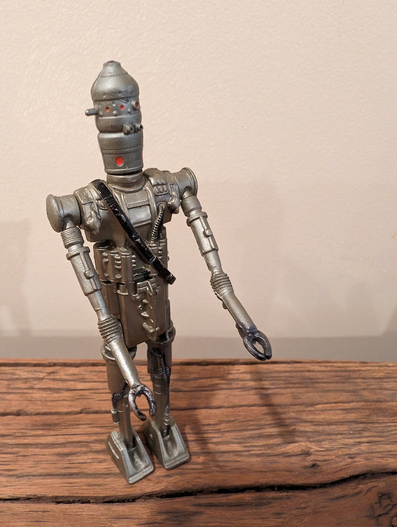 Peut inclure: Une figurine d'action de robot argent&eacute;e et noire avec un design d&eacute;taill&eacute;. Le robot a une t&ecirc;te en forme de d&ocirc;me avec des yeux rouges et une sangle noire sur la poitrine.
