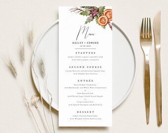 May include: A white wedding menu card with a watercolor illustration of holly berries and oranges. The menu includes starters, second course, entree, and dessert. The text reads "Menu" and "Hailey + Edward 10.10.2021".