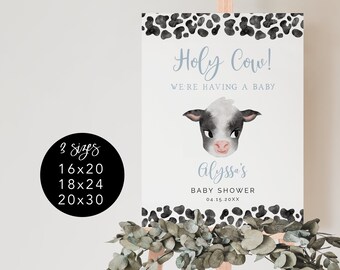 May include: A white sign with black cow print border and a black and white cow illustration. The sign says "Holy Cow! We're having a baby" and "Alyssa's Baby Shower 04.15 20XX". The sign is on a wooden easel.