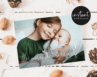 May include: A Christmas card featuring a photo of two children, a girl and a baby, hugging. The card has a white background with the text "the more the merrier" written in cursive. The text "Love, The Reason Family Christmas 2021" is written below the cursive text.