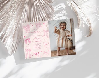 May include: A birthday invitation with a photo of a smiling child. The invitation features pink bow illustrations and text that reads "Adlyas 1st Birthday". The invitation is on a white surface with decorative elements.