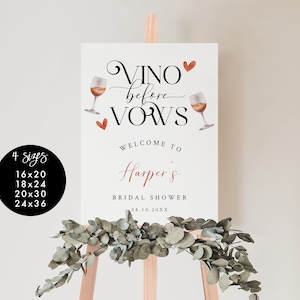 Pode incluir: Um cartaz branco com o texto "VINO before VOWS" em letra cursiva preta com duas ta&ccedil;as de vinho e cora&ccedil;&otilde;es vermelhos. O texto "WELCOME TO Harper's BRIDAL SHOWER 08.10.20XX" est&aacute; em preto e vermelho. O cartaz est&aacute; em um cavalete de madeira.