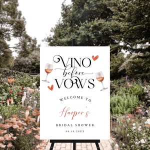 Pode incluir: Um cartaz branco com o texto "Vino before vows" em escrita cursiva com um cora&ccedil;&atilde;o vermelho e duas ta&ccedil;as de vinho com cora&ccedil;&otilde;es vermelhos. O texto "Welcome to Harper's Bridal Shower 08.10.20XX" est&aacute; abaixo do texto principal.
