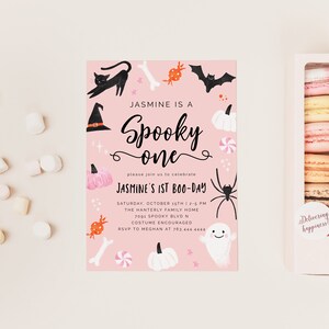 May include: Pink Halloween party invitation with black and white illustrations of a witch's hat, a black cat, a spider, a ghost, candy, pumpkins, and bones. The text reads "Jasmine is a Spooky One" and "Jasmine's 1st Boo-Day".