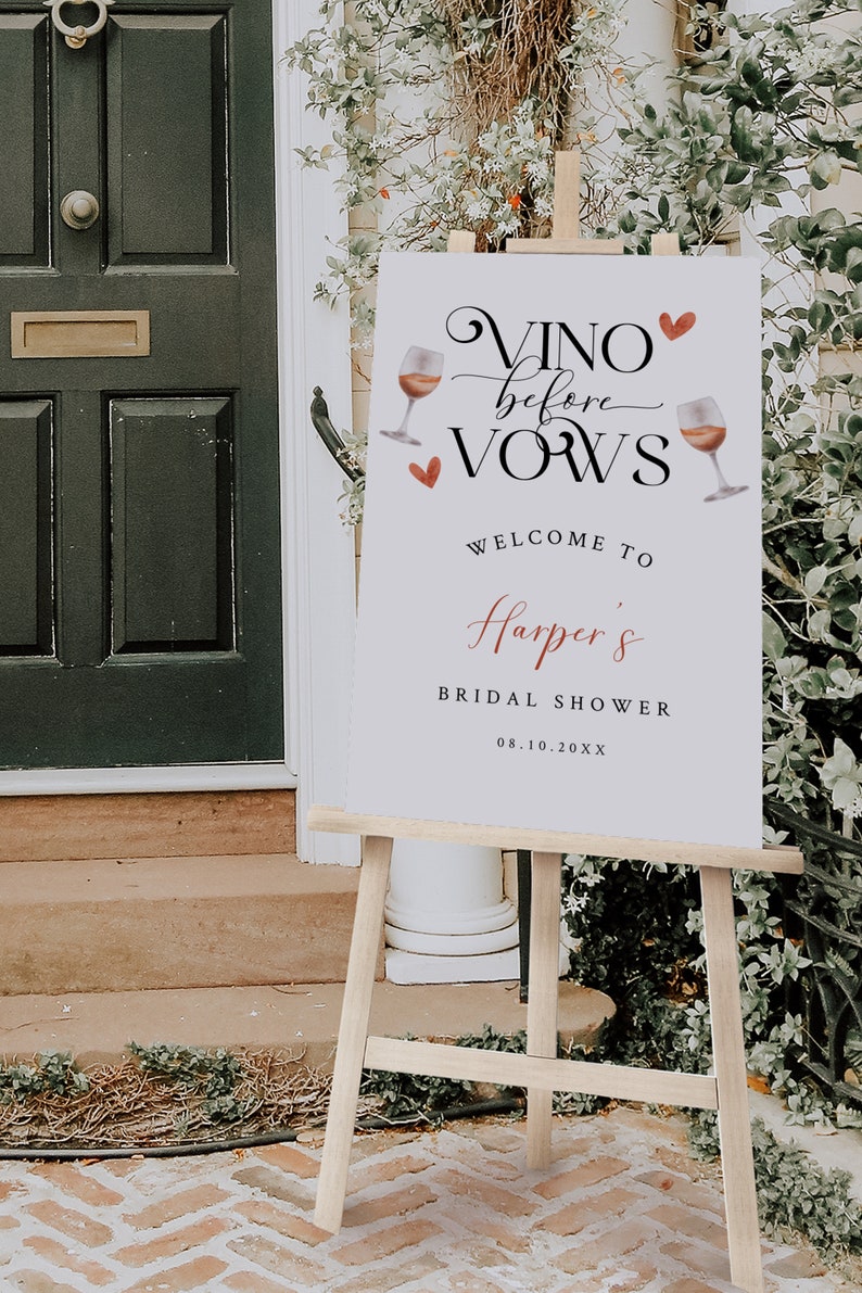 Pode incluir: Um cartaz branco com texto preto que diz "Vino before Vows" com um cora&ccedil;&atilde;o vermelho e ilustra&ccedil;&otilde;es de ta&ccedil;as de vinho. O cartaz tamb&eacute;m diz "Welcome to Harper's Bridal Shower 08.10.20XX". O cartaz est&aacute; em um cavalete de madeira.