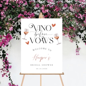 Pode incluir: Uma placa branca com o texto "Vino before Vows" em caligrafia preta. A placa tamb&eacute;m inclui duas ta&ccedil;as de vinho com vinho tinto e cora&ccedil;&otilde;es. O texto "Welcome to Harper's Bridal Shower 08.10.20XX" tamb&eacute;m est&aacute; na placa.