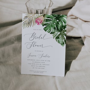 Puede incluir: Una invitaci&oacute;n de despedida de soltera blanca con un tema tropical. La invitaci&oacute;n presenta una ilustraci&oacute;n de acuarela de hojas de palma verdes y una flor rosa. El texto de la invitaci&oacute;n dice: "&Uacute;nete a nosotros para una despedida de soltera en honor a Jessica Sanders. S&aacute;bado, 25 de julio a las 3:00 p. m. Flamingo Cafe 7344 98th Ave SE, Chicago RSVP a Chelsea al 763.446.2944 Jessica est&aacute; registrada en Pottery Barn."