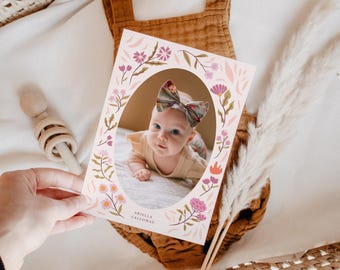 May include: A pink floral photo card with an oval cutout featuring a baby girl wearing a pink and white bow. The text "Ariella Calloway" is printed below the photo.