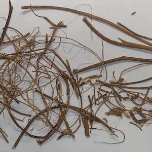 May include: A collection of dried, brown, and tan roots and stems, possibly herbs or botanicals, scattered on a white surface. The pieces vary in thickness and length, with some appearing more fibrous.