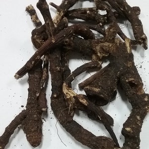 May include: A collection of dried, dark brown roots with a rough, textured appearance. The roots vary in size and shape, with some having a gnarled, branch-like structure. The image is a close-up, showing the details of the roots against a white background.