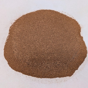May include: A close-up of a pile of brown powder on a white surface. The powder is fine and evenly distributed.