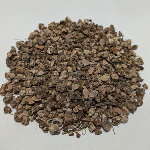 May include: A close-up of a pile of brown and reddish-brown bark chips. The chips are irregular in shape and size, and some have a rough texture.