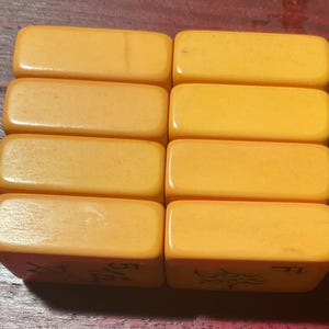 May include: Eight rectangular, light orange tiles are arranged in two rows of four. The tiles have rounded edges and appear to be made of a smooth, solid material. The bottom of each tile has an etched design and numbers.