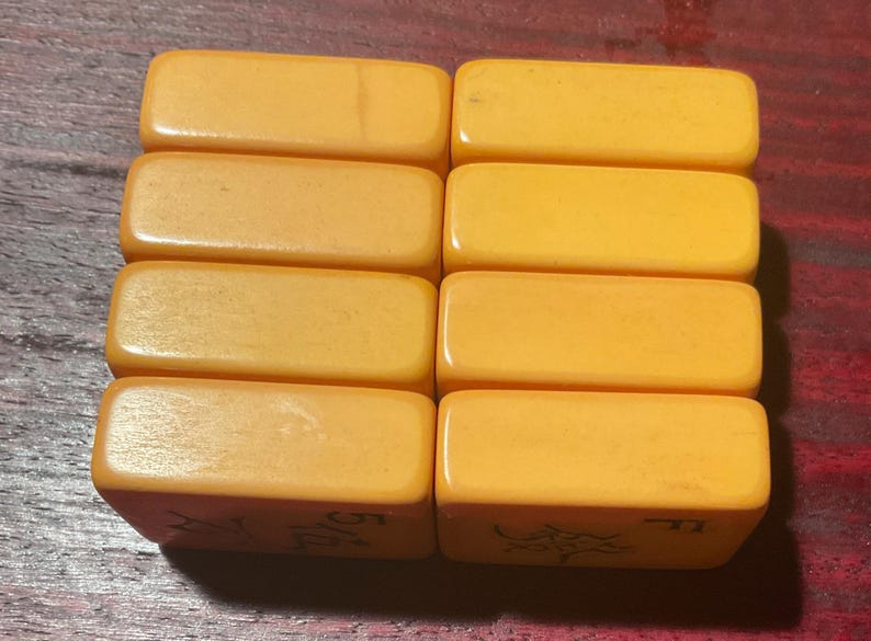 May include: Eight rectangular, light orange tiles are arranged in two rows of four. The tiles have rounded edges and appear to be made of a smooth, solid material. The bottom of each tile has an etched design and numbers.