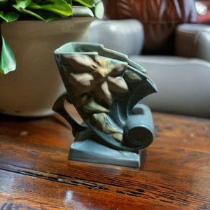 May include: A blue and green ceramic vase with a floral design. The vase is shaped like a curved horn and has a wide opening at the top.
