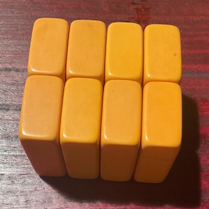 May include: Eight rectangular, orange-yellow game tiles are arranged in two rows of four. The tiles have rounded corners and a smooth, glossy finish. The background is a dark, reddish-brown wooden surface.