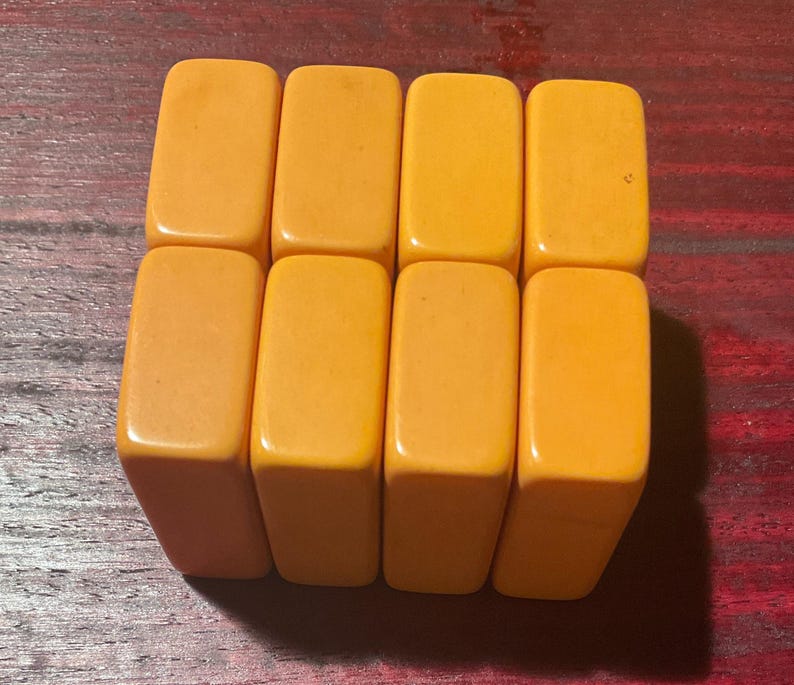 May include: Eight rectangular, orange-yellow game tiles are arranged in two rows of four. The tiles have rounded corners and a smooth, glossy finish. The background is a dark, reddish-brown wooden surface.