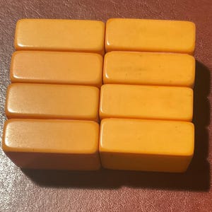 Puede incluir: Ocho baldosas rectangulares de baquelita de color &aacute;mbar dispuestas en dos filas de cuatro. Las baldosas tienen bordes redondeados y un acabado brillante, lo que sugiere una est&eacute;tica vintage o antigua. Las baldosas se muestran sobre una superficie marr&oacute;n rojiza oscura.