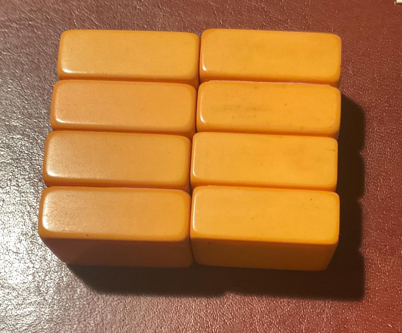 Puede incluir: Ocho baldosas rectangulares de baquelita de color &aacute;mbar dispuestas en dos filas de cuatro. Las baldosas tienen bordes redondeados y un acabado brillante, lo que sugiere una est&eacute;tica vintage o antigua. Las baldosas se muestran sobre una superficie marr&oacute;n rojiza oscura.