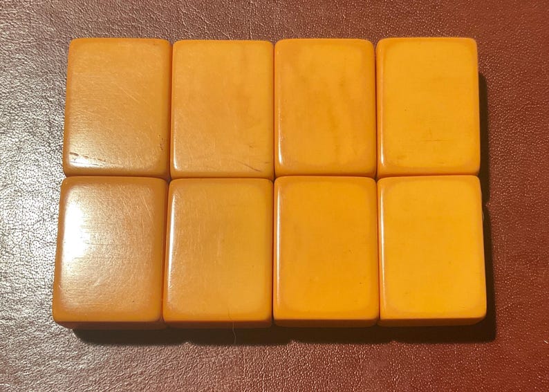 Puede incluir: Ocho baldosas rectangulares de color &aacute;mbar dispuestas en dos filas. Las baldosas tienen una superficie lisa y brillante con sutiles variaciones de tono. Las baldosas son probablemente componentes de un juego.