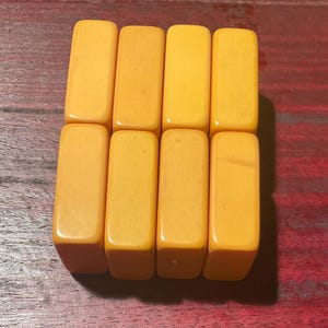 May include: Eight rectangular, amber-colored game tiles arranged in two rows of four. The tiles have rounded edges and a smooth, glossy finish. The background is a dark, reddish-brown wooden surface.