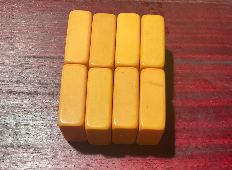 May include: Eight rectangular, amber-colored game tiles arranged in two rows of four. The tiles have rounded edges and a smooth, glossy finish. The background is a dark, reddish-brown wooden surface.