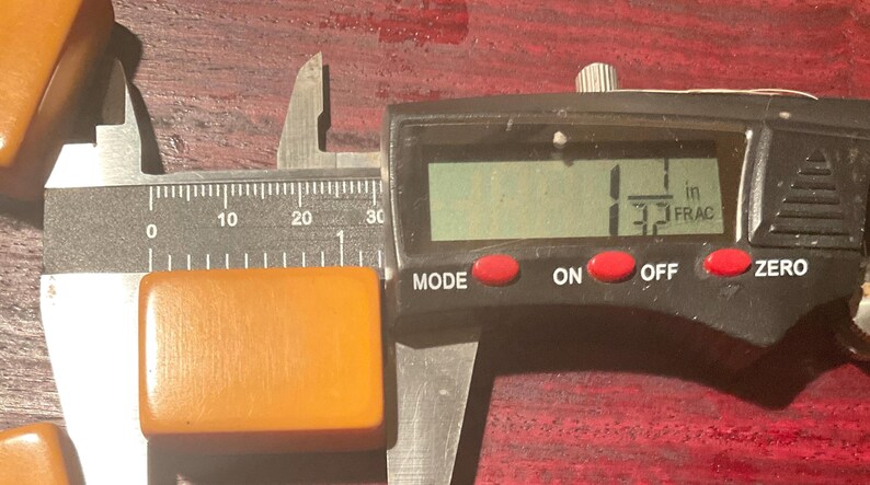 May include: A rectangular, amber-colored object is measured with a digital caliper. The caliper displays a measurement of 1.3 inches. The object is positioned on a dark, reddish-brown surface.