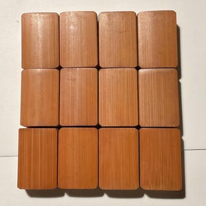 May include: A set of twelve rectangular mahjong tiles arranged in a grid of three rows and four columns. Each tile features a smooth, light brown bamboo wood grain texture with rounded corners and a flat, uniform surface on the front side.