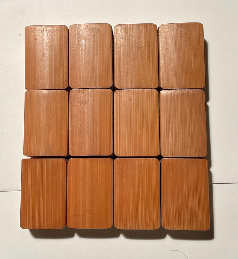 May include: A set of twelve rectangular mahjong tiles arranged in a grid of three rows and four columns. Each tile features a smooth, light brown bamboo wood grain texture with rounded corners and a flat, uniform surface on the front side.