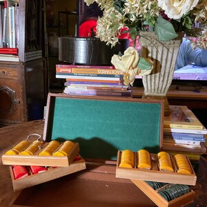 Pu&ograve; includere: Una valigetta vintage in similpelle marrone con interno in feltro verde, contenente diversi vassoi di fiches gialle, rosse e verdi. La valigetta &egrave; aperta, mostrando le fiches in vassoi di legno. Sullo sfondo &egrave; visibile una composizione floreale decorativa.