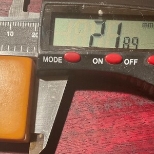 May include: A light brown rectangular object is measured with a digital caliper. The caliper displays a measurement of 21 mm by 18.9 mm. The object has a smooth, slightly textured surface.