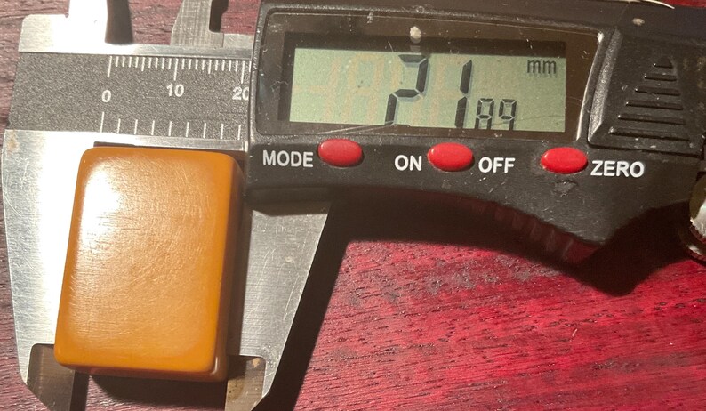 May include: A light brown rectangular object is measured with a digital caliper. The caliper displays a measurement of 21 mm by 18.9 mm. The object has a smooth, slightly textured surface.