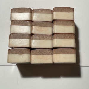 May include: A grid of twelve rectangular blocks arranged in four rows and three columns. Each block features a two-toned design with a textured, light brown wooden top section and a smooth, solid off-white base section, creating a uniform appearance.
