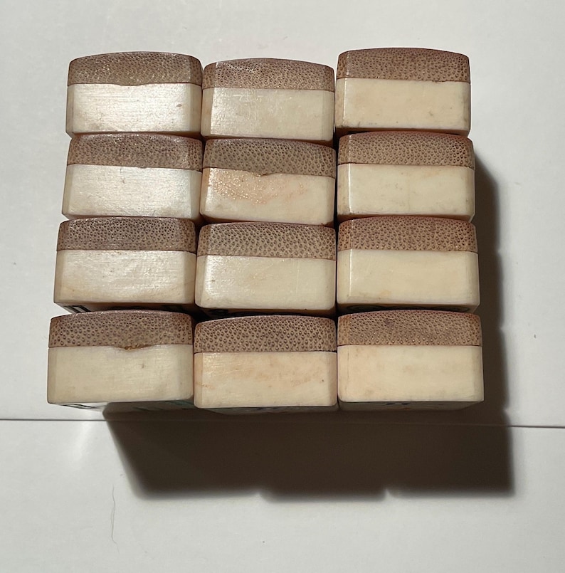 May include: A grid of twelve rectangular blocks arranged in four rows and three columns. Each block features a two-toned design with a textured, light brown wooden top section and a smooth, solid off-white base section, creating a uniform appearance.