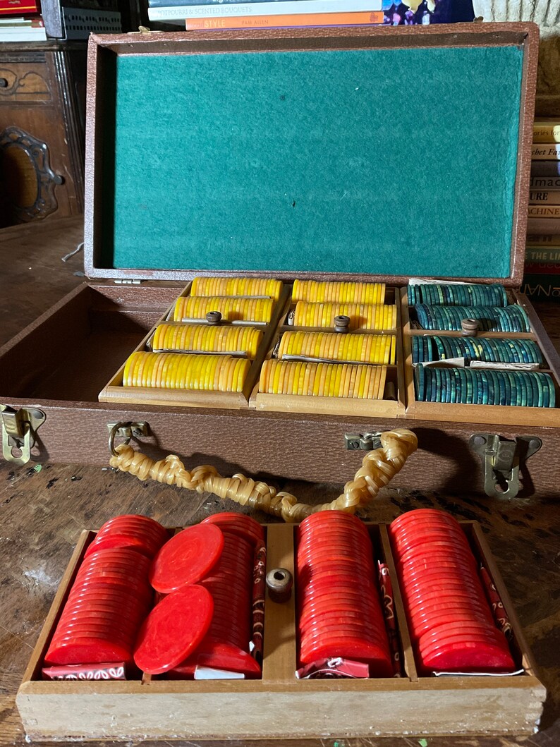 Pu&ograve; includere: Una valigetta da poker vintage in legno aperta, che mostra fiches gialle, verdi e rosse. L'interno &egrave; in feltro verde e ha un manico in corda intrecciata. La valigetta &egrave; su una superficie di legno.