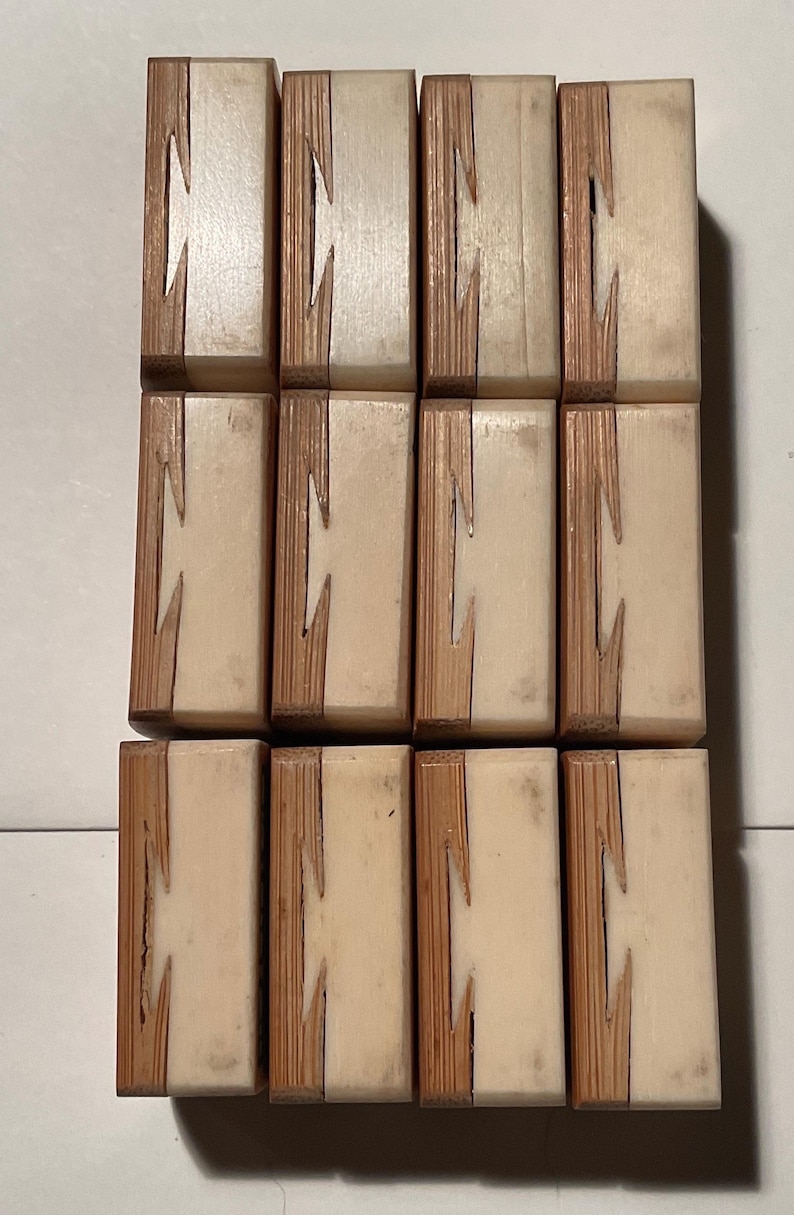 May include: A collection of twelve rectangular wooden blocks arranged in a grid of three rows and four columns. Each block features a two-tone design with a light cream-colored section joined to a textured brown wood section by a zigzag joint.